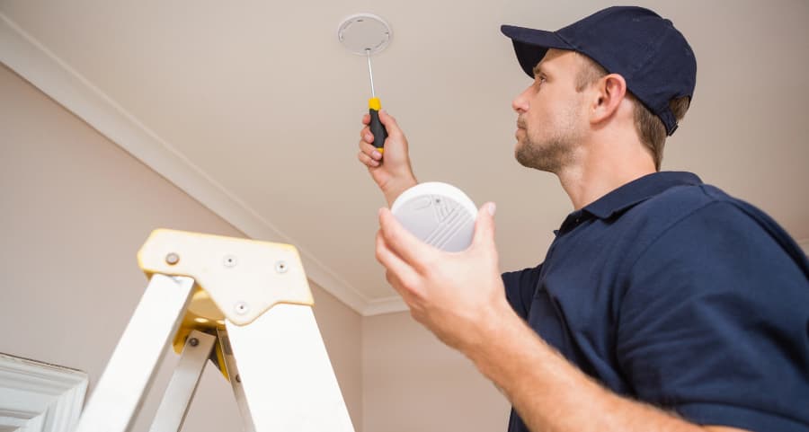 Man placing fire alarm on ceiling